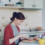 Happy young mother cooking vegetables cutting tomatoes and talking to her cheerful daughter in the kitchen at home. Family, cook, and people concept